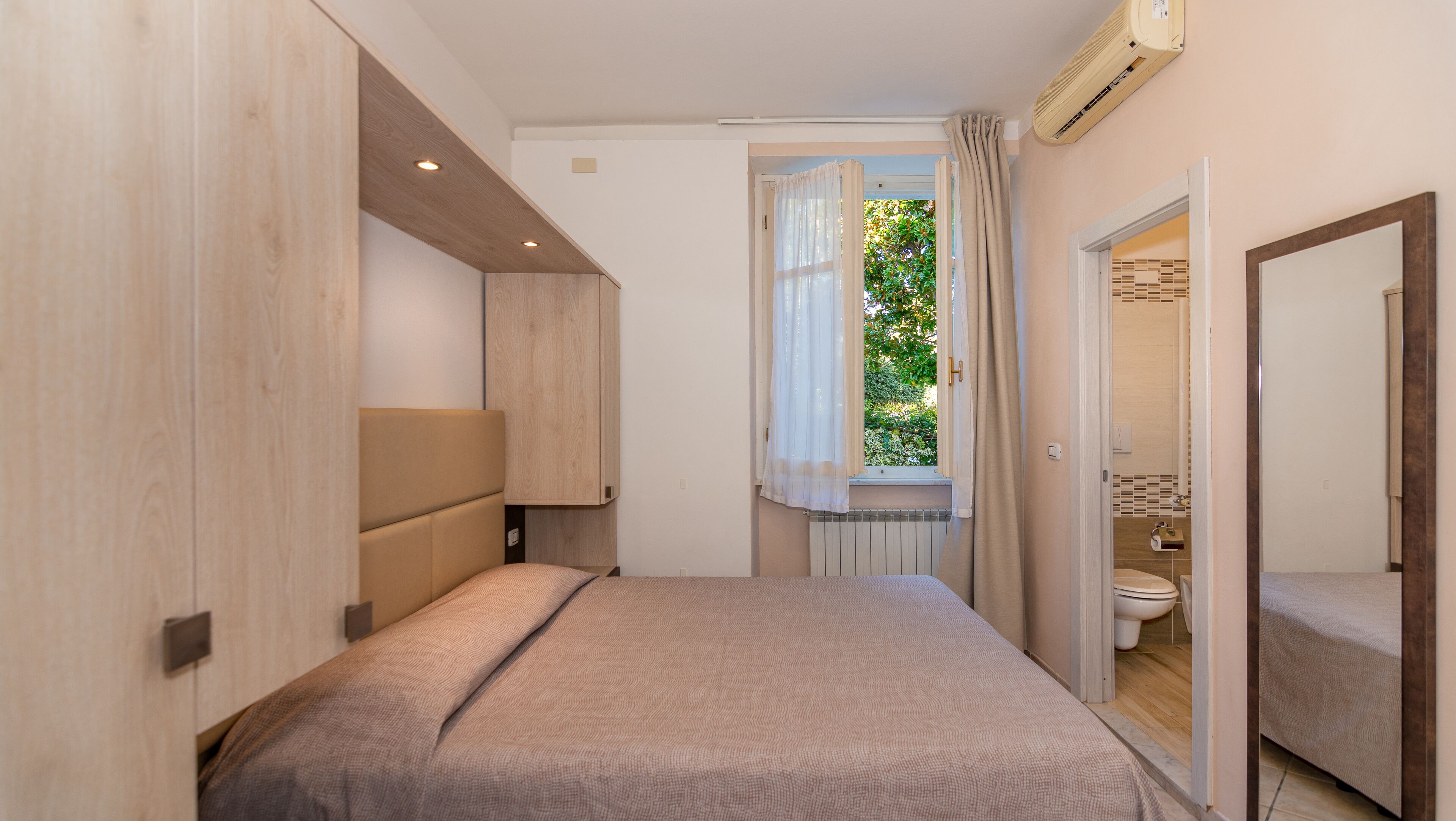 A bedroom with a bed, a window with curtains, a radiator, and an air conditioning unit.