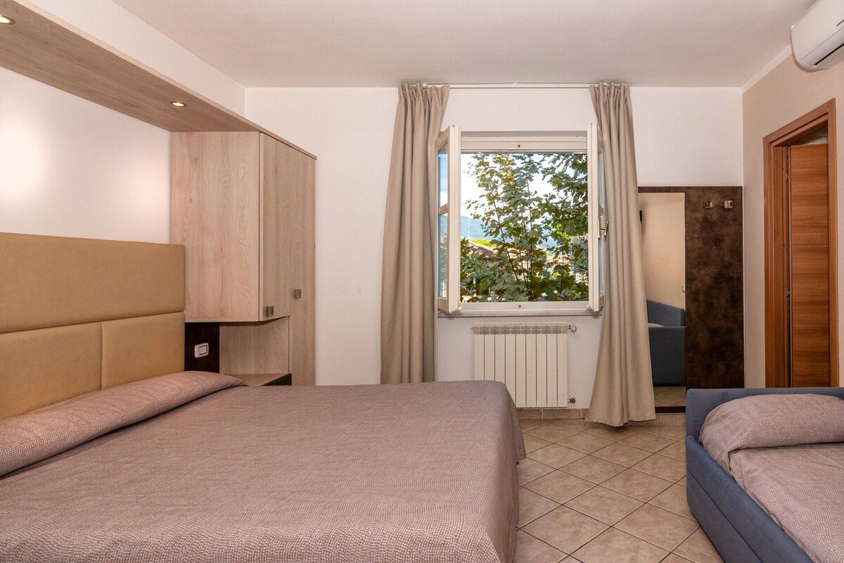 A bedroom with two beds, a window with curtains, a radiator, and a door.