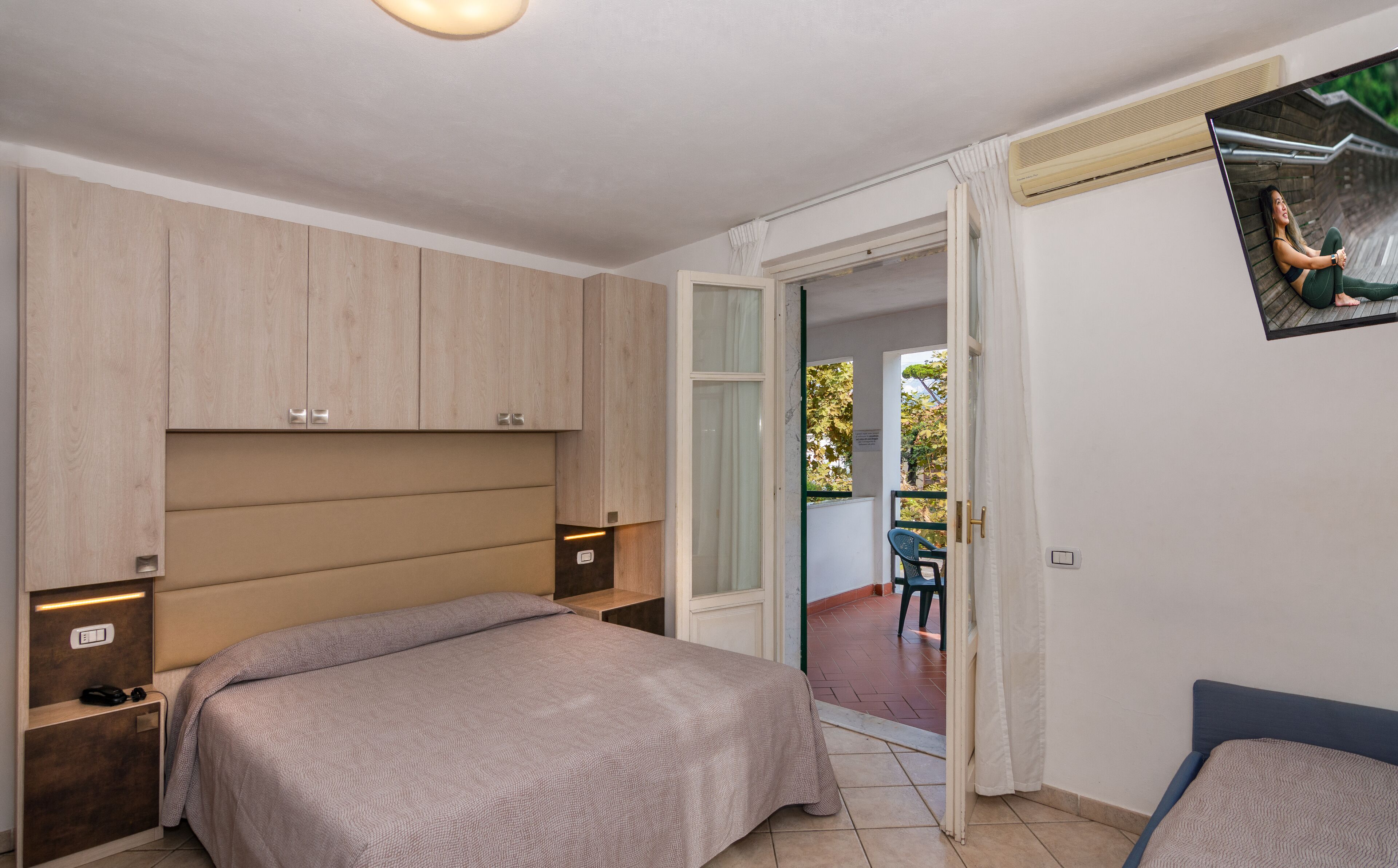 A bedroom with a bed, a desk, a chair, and a sliding glass door leading to an outdoor area.