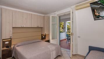 A bedroom with a bed, a desk, a chair, and a sliding glass door leading to an outdoor area.