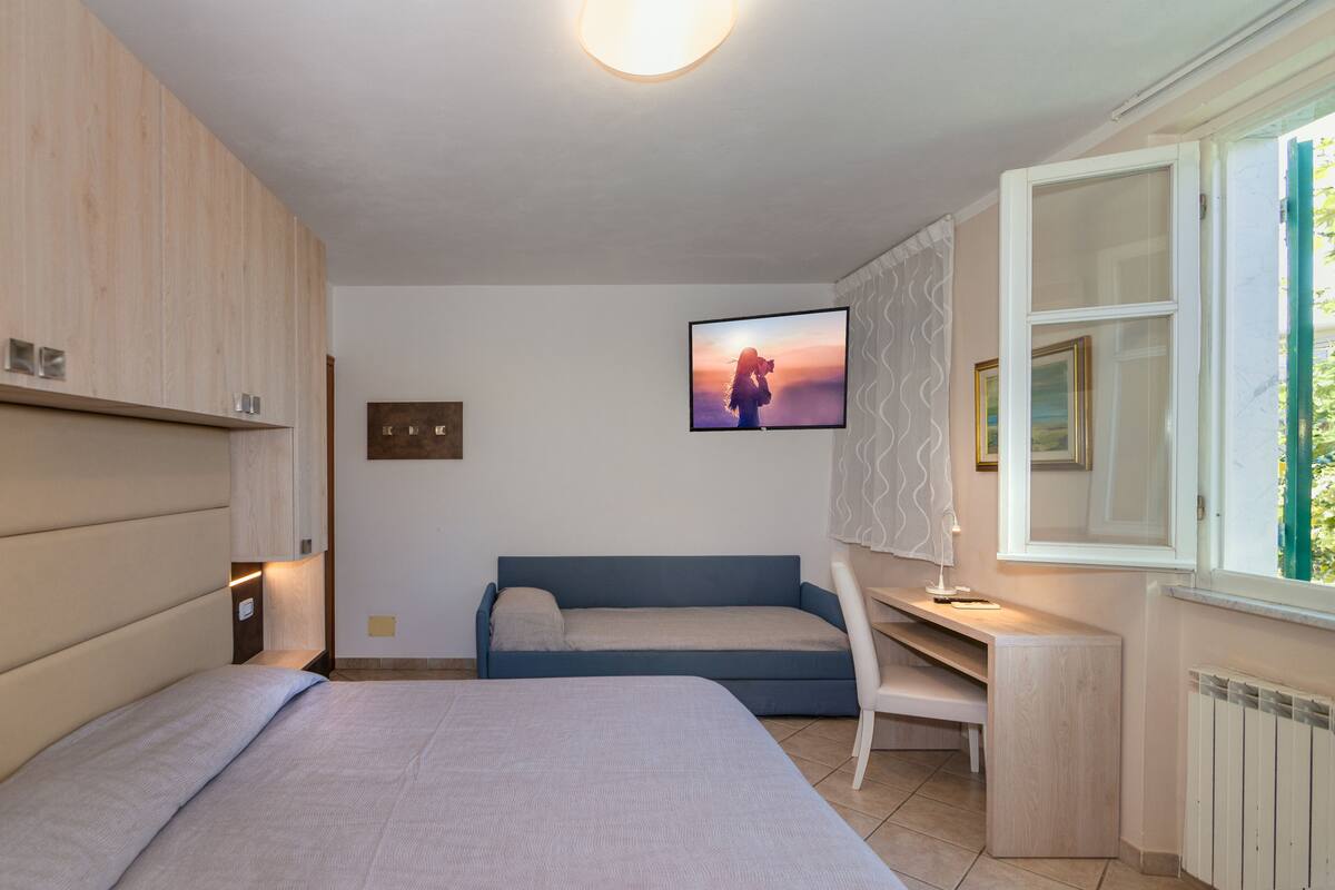 A bedroom with a bed, a desk, a blue sofa, and a wall-mounted TV.