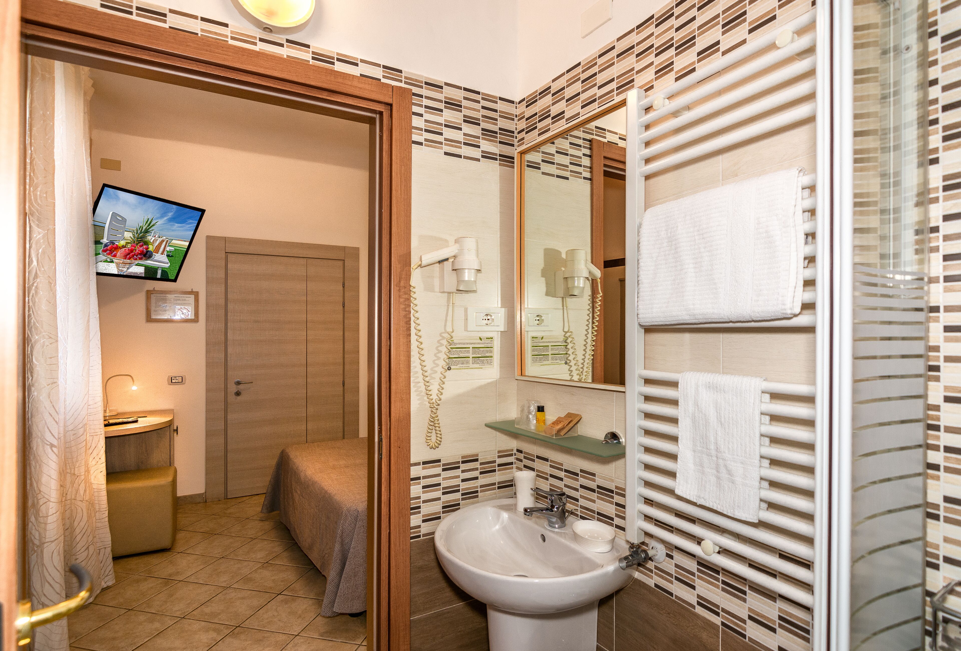 A bathroom with a sink, mirror, towel rack, and a television on the wall.