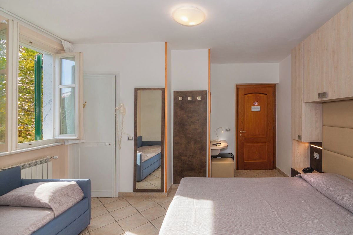 A bedroom with a bed, a bedside table, a mirror, a window, and a door.