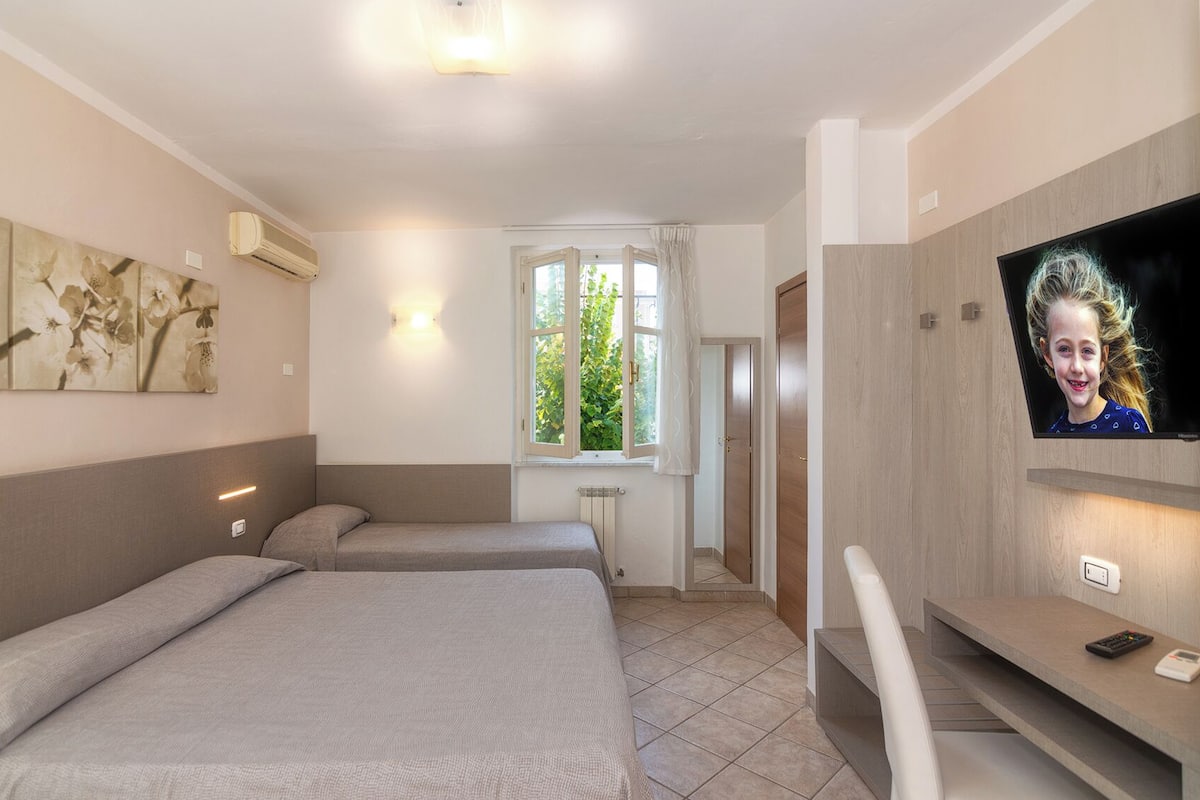 A hotel room with two beds, a TV, a window with curtains, and a radiator.