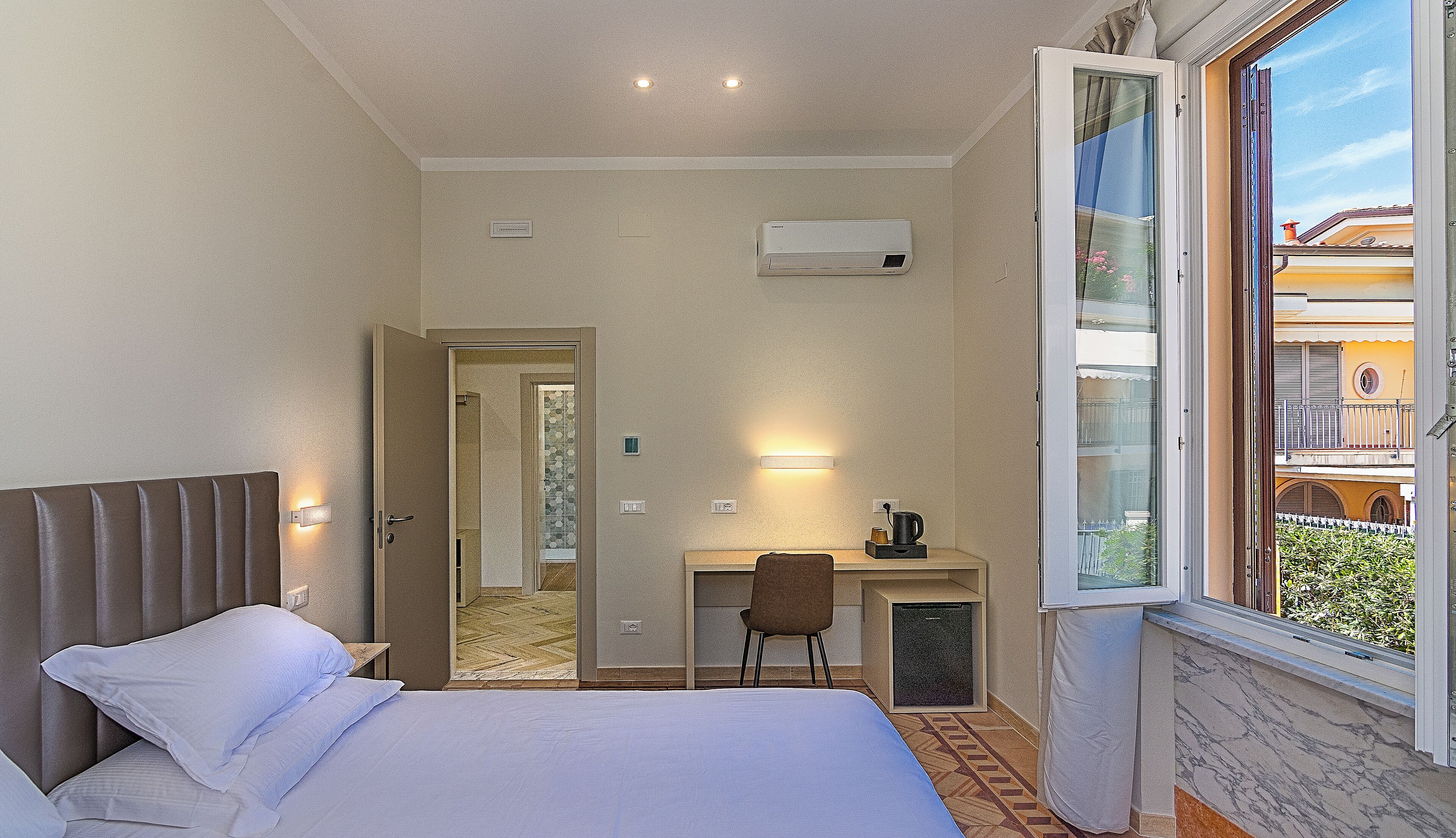 Une chambre d’hôtel équipée d’un lit, d’un bureau, d’une chaise et d’une fenêtre donnant sur des immeubles.