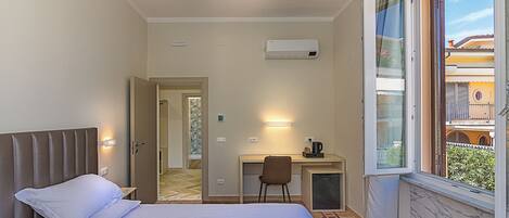 A hotel room with a bed, a desk, a chair, and a window with a view of buildings.