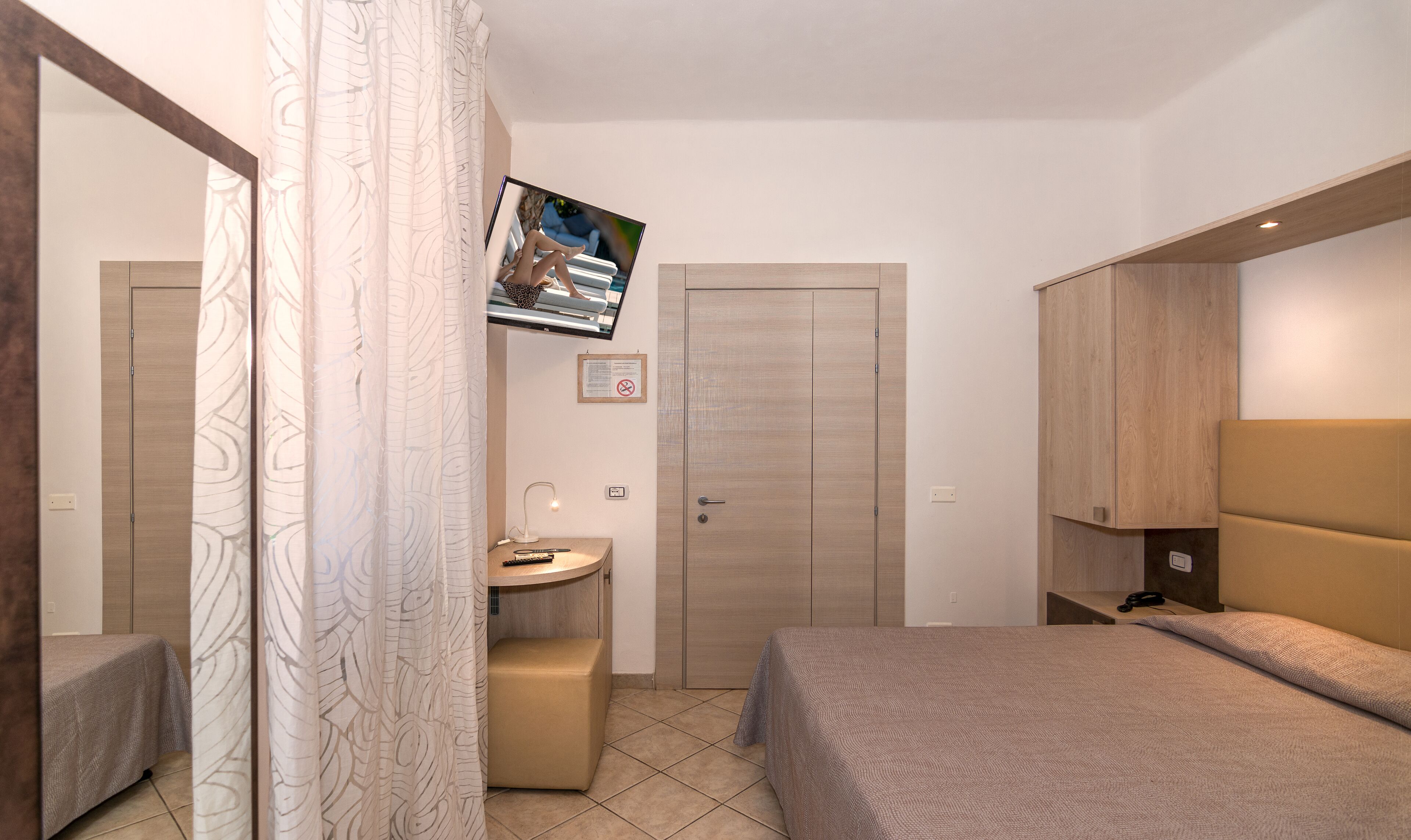 Een hotelkamer met een bed, bureau, televisie aan de muur en een kledingkast.