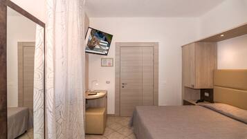 A hotel room with a bed, a desk, a television mounted on the wall, and a wardrobe.