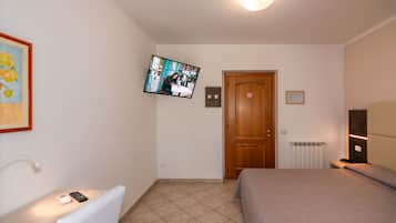 Habitación de hotel con cama, televisor montado en la pared, mesita de noche con control remoto y puerta con un cartel.