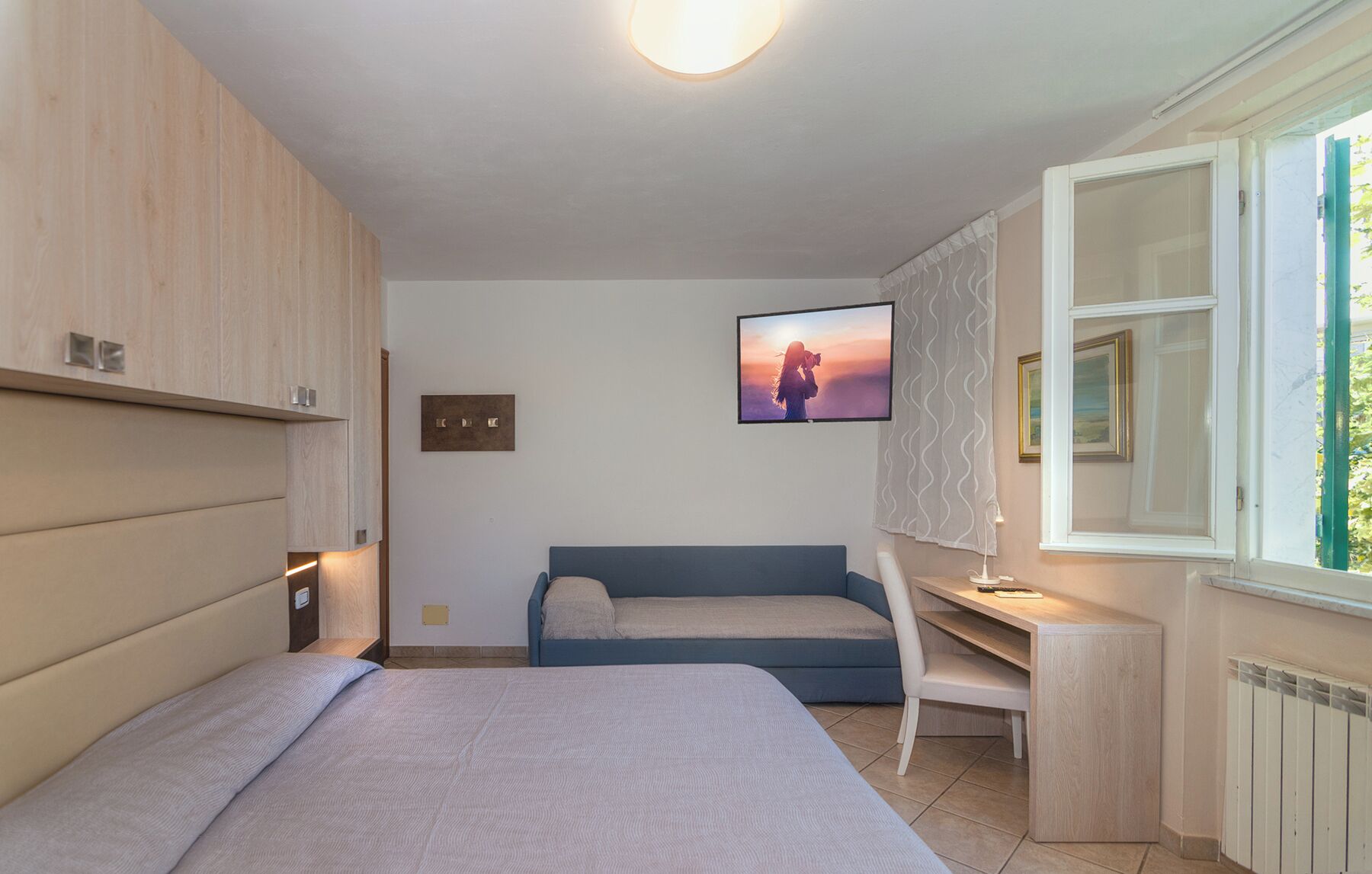 Une chambre à coucher avec un lit, un bureau, une chaise, un canapé, une télévision et une fenêtre.