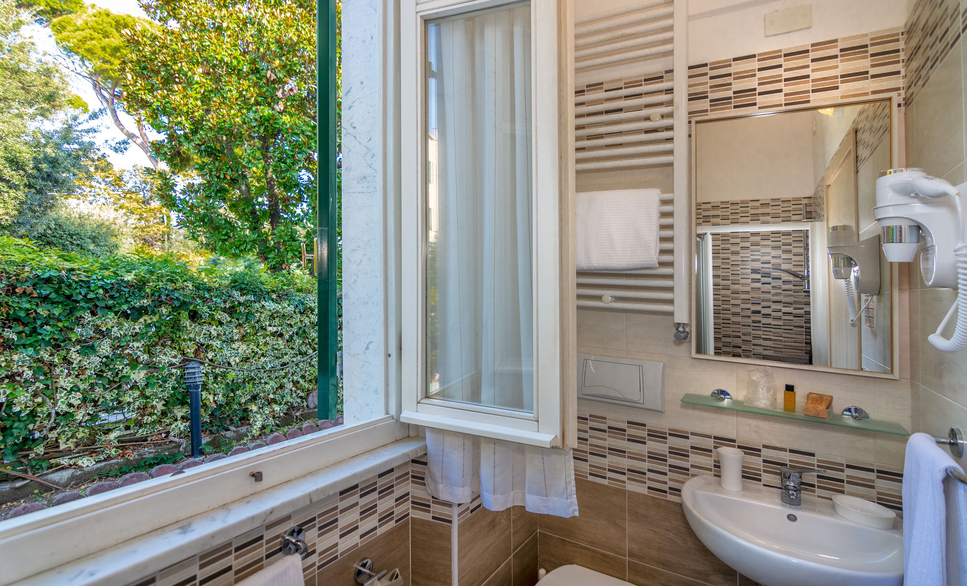 Un baño con ventana, lavamanos, espejo y perchero para toallas.