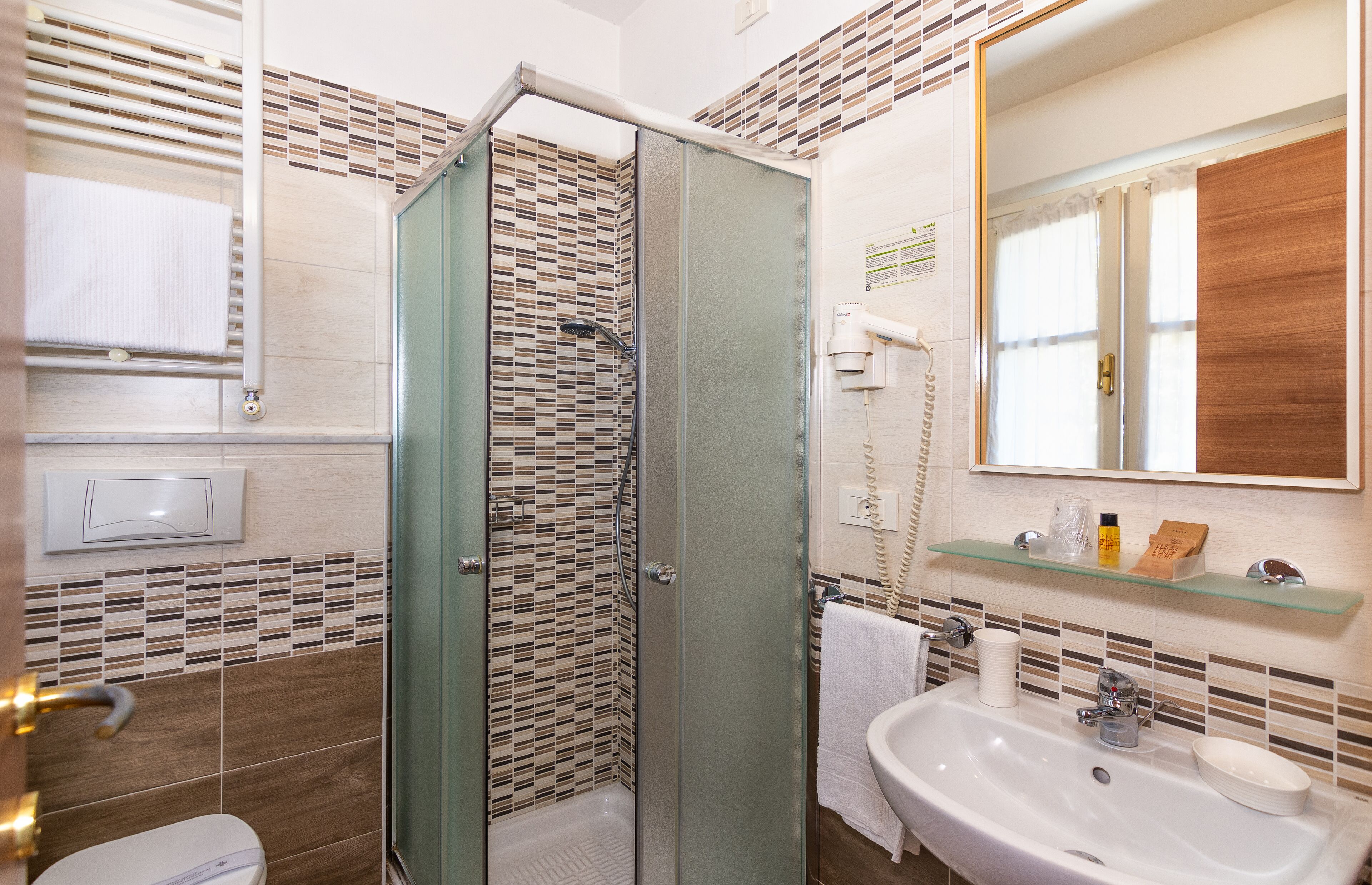 Un bagno con box doccia in vetro, lavandino con specchio e portasciugamani.