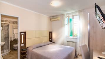 Camera d'albergo con un letto, un comodino, una sedia, bagno con doccia e una finestra con tende.