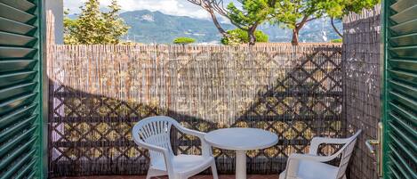 Un patio con dos sillas de plástico blancas y una pequeña mesa redonda, una valla de bambú, y vistas a montañas y árboles.