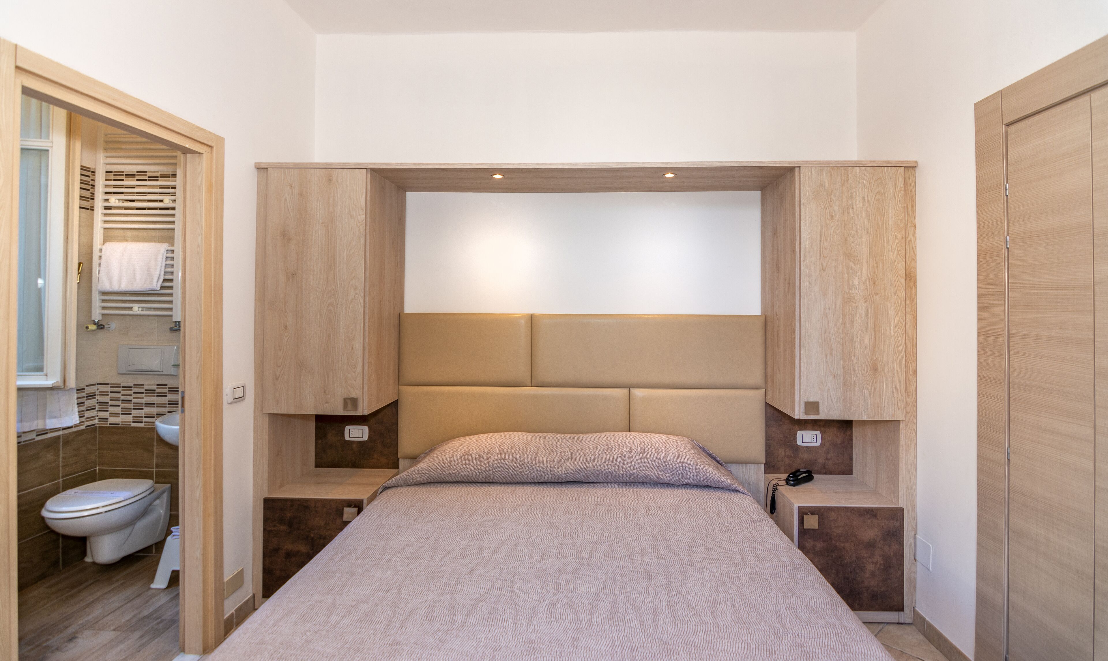 A modern bedroom with a bed, wooden headboard, bedside tables, and a built-in wardrobe.