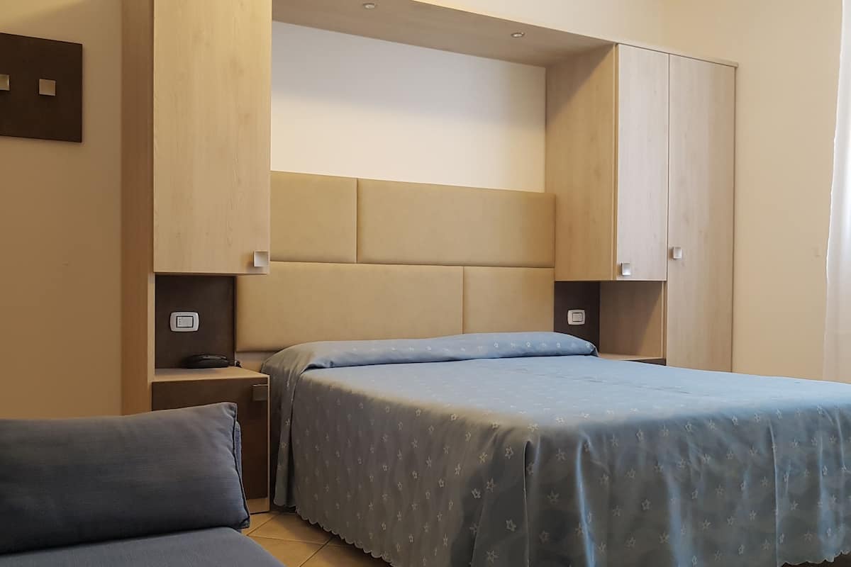A bedroom with two beds, a sofa, and built-in wardrobes.