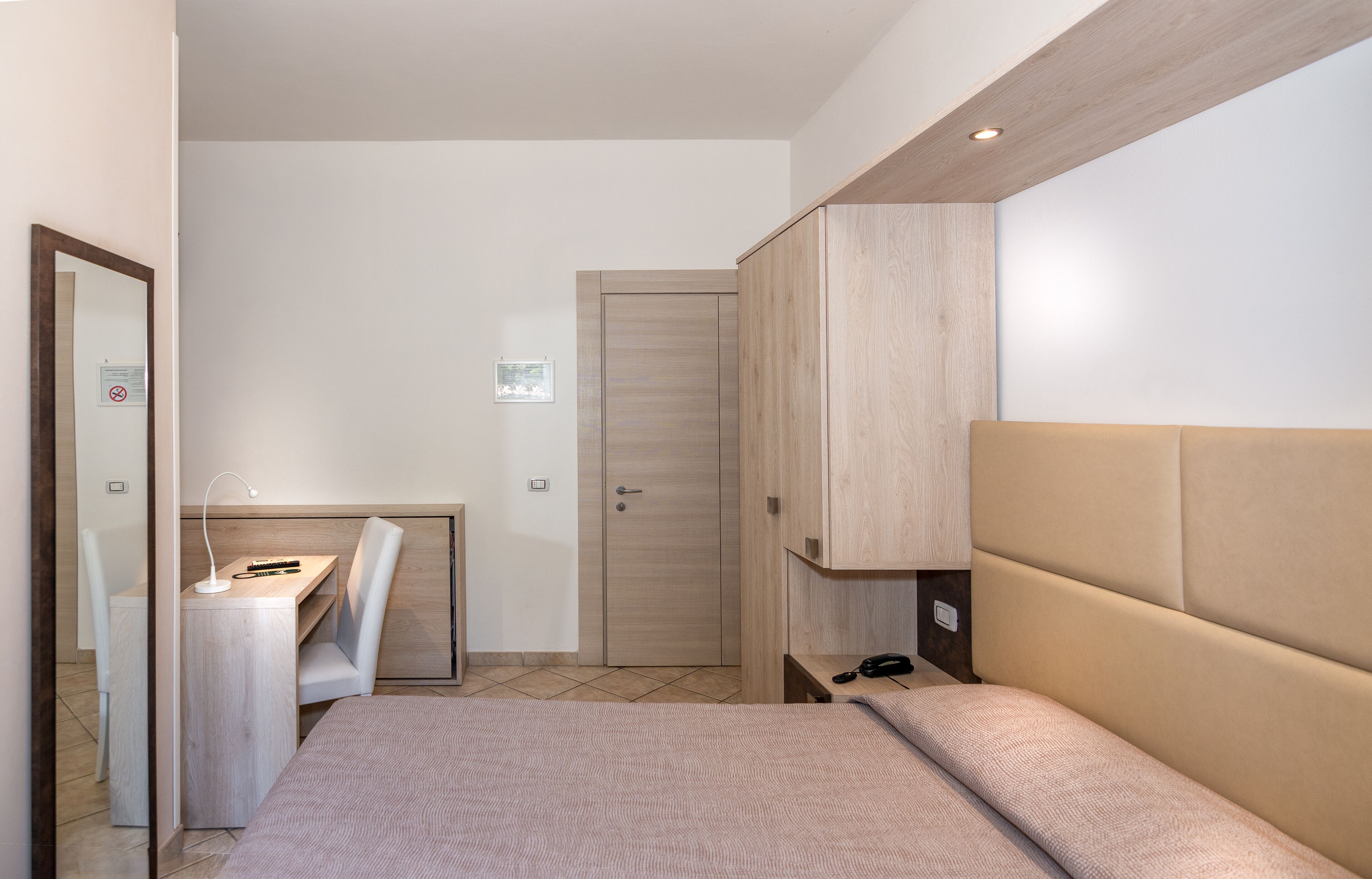 A bedroom with a bed, a desk, a chair, a wardrobe, and a door.