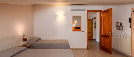 A bedroom with two beds, a bedside table with a lamp, a wall-mounted light, a mirror, and a door leading to another room.