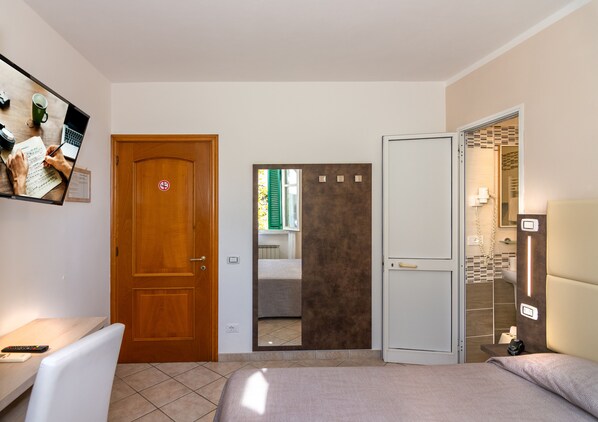 Habitación de hotel con una cama, un escritorio con silla, un espejo y un baño visible a través de una puerta abierta.