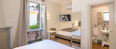 Habitación de hotel con cama, una mesita, una silla, televisor y baño a la vista a través de una puerta abierta.