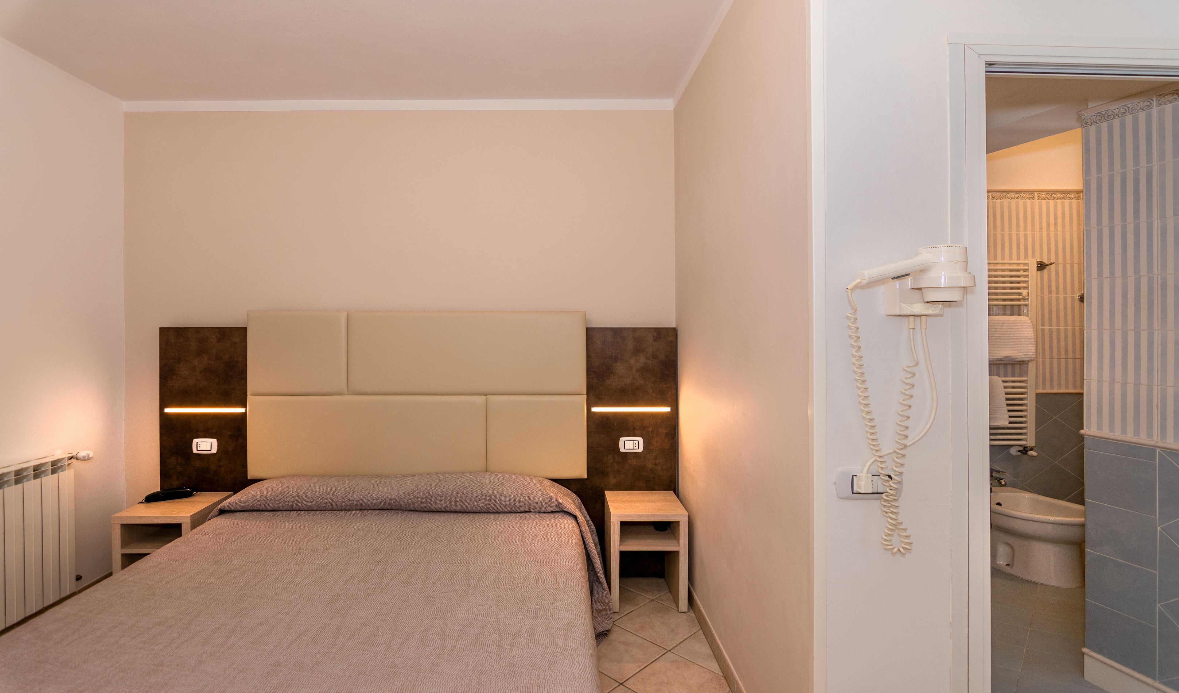 Ein Hotelzimmer mit einem Bett, Nachttischen, einem Telefon und einem durchgegangenen Tür sichtbaren Badezimmer.