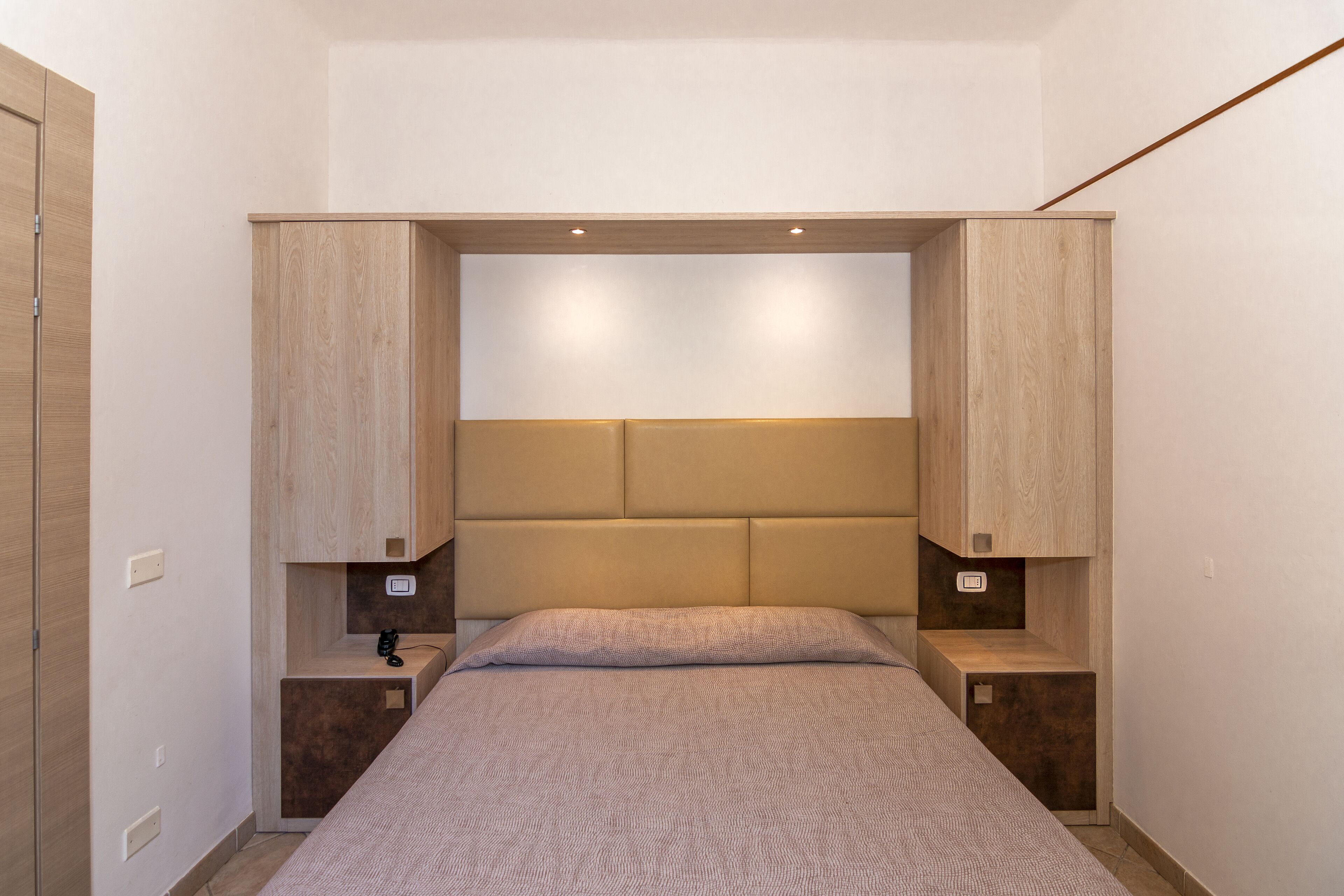 Une chambre à coucher comprenant un lit, une tête de lit intégrée, des tables de chevet et une armoire.