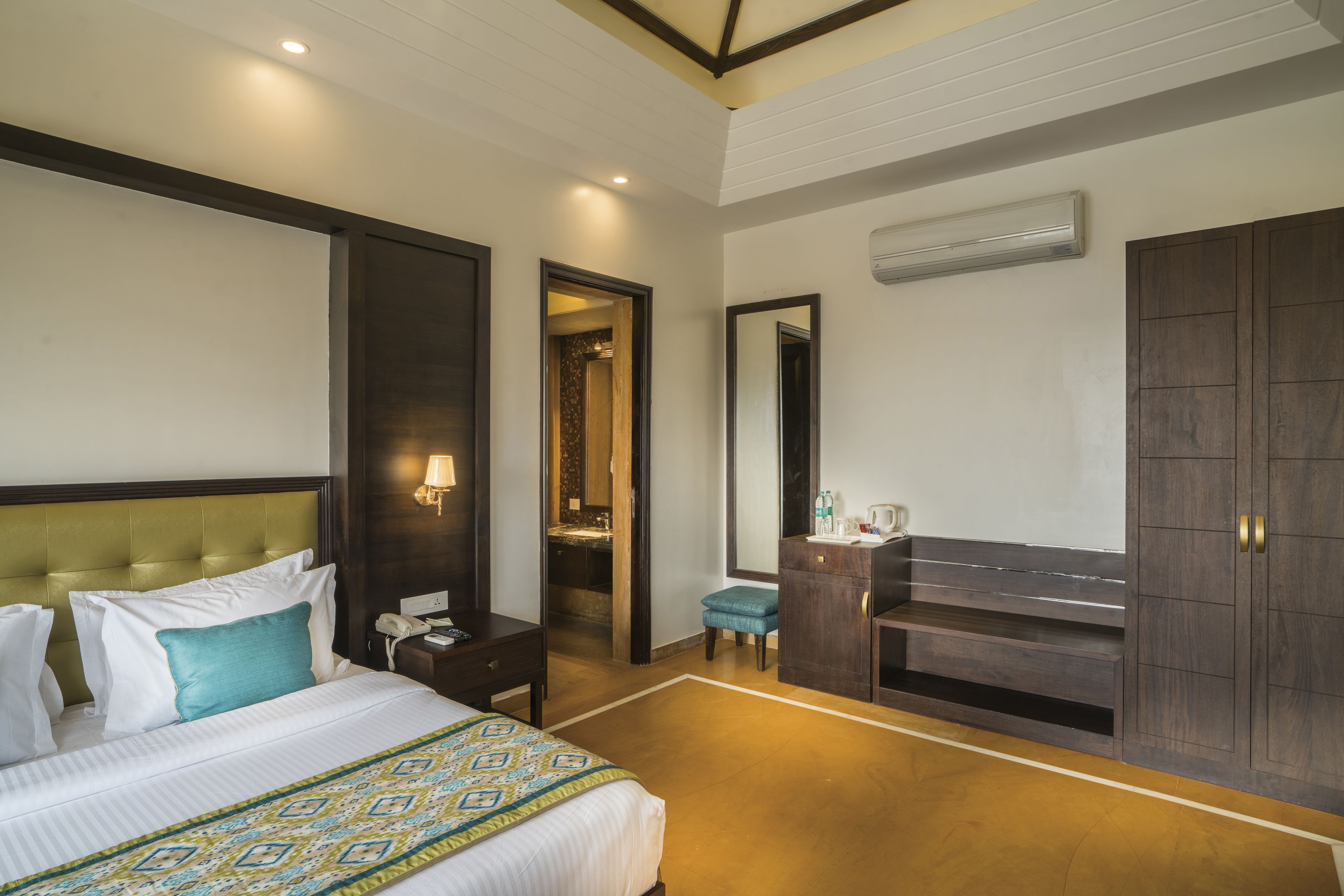 A hotel room with a large bed, a nightstand, a desk, a mirror, and a wardrobe.