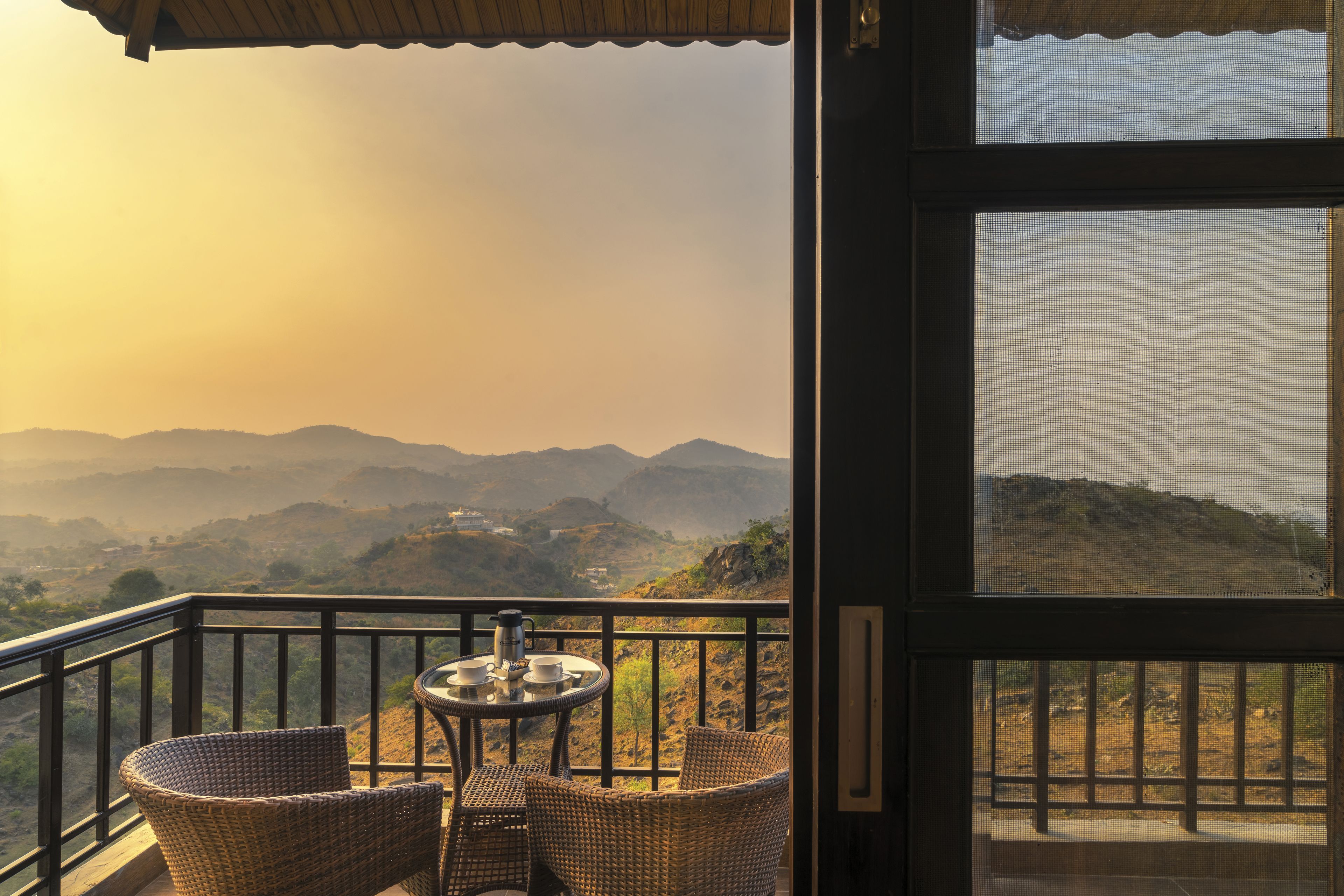 A balcony with wicker furniture and a table, overlooking a mountainous landscape.