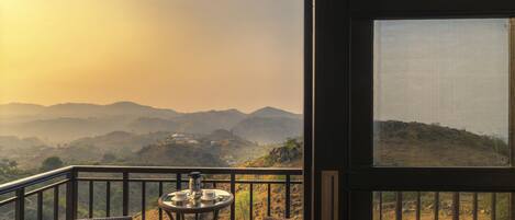 A balcony with wicker furniture and a table, overlooking a mountainous landscape.