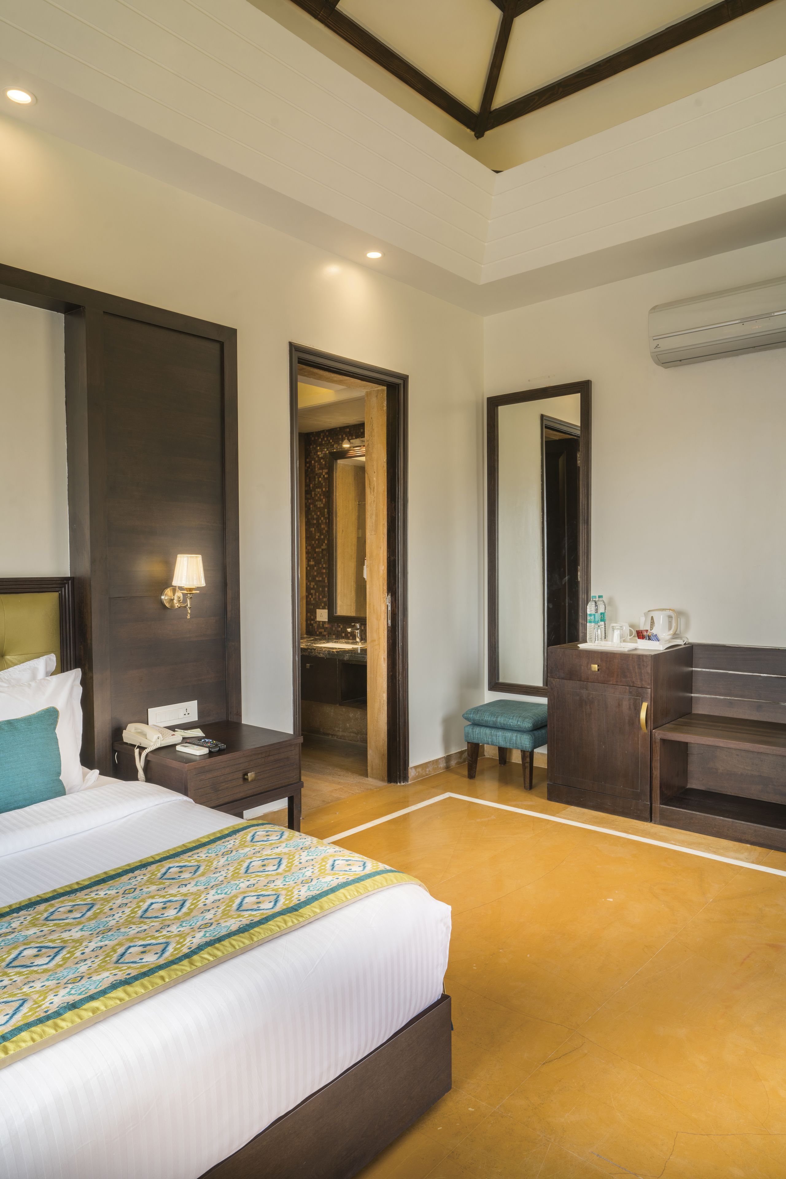 A hotel room with a large bed, a desk with a lamp, a mirror, and a wardrobe.