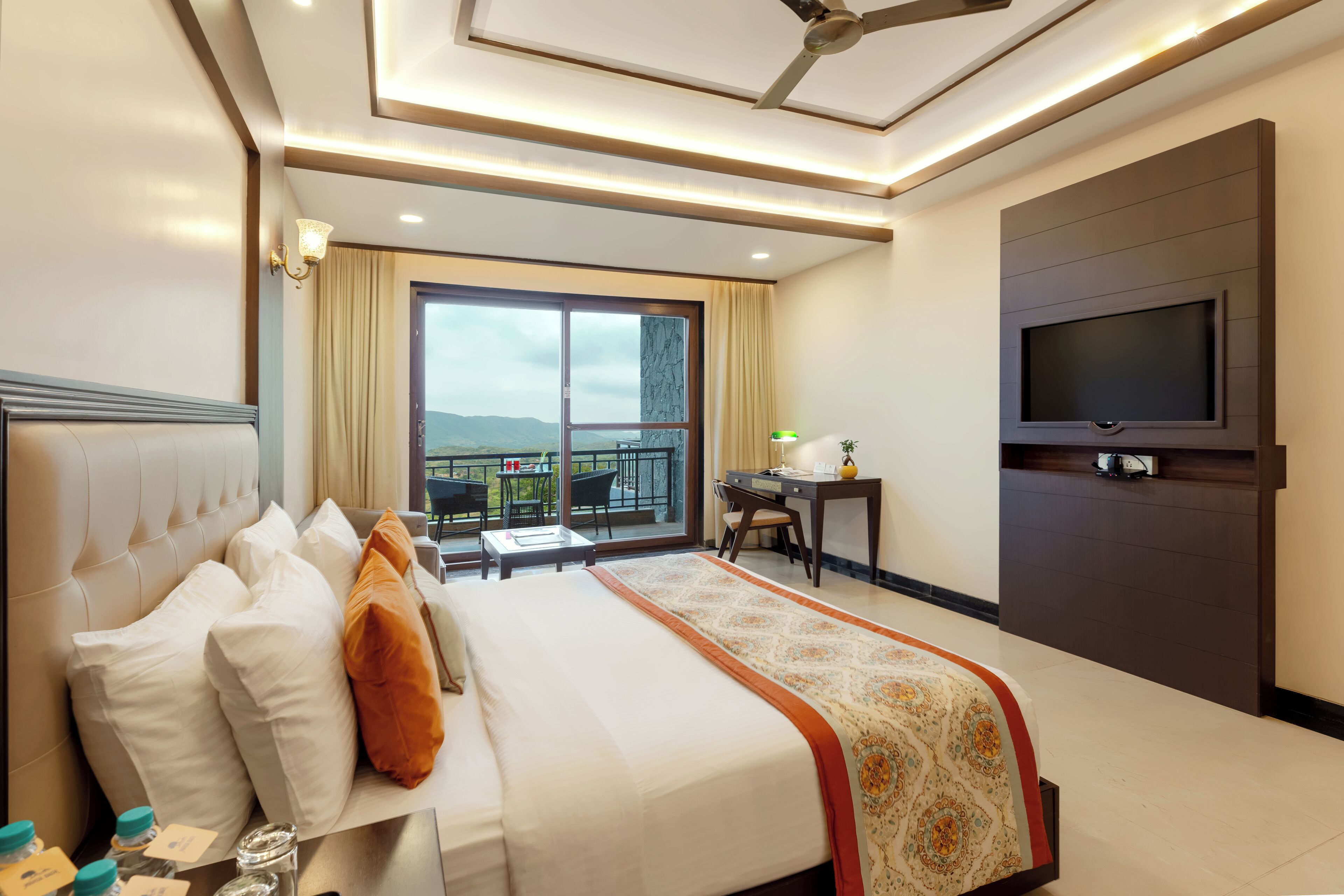 Habitación de hotel con cama, escritorio, televisor y balcón con vistas.