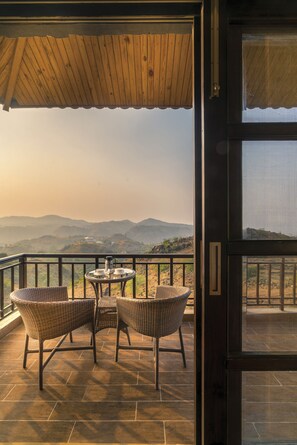 Un balcón con sillas de mimbre y una mesa, con vista a un paisaje montañoso.