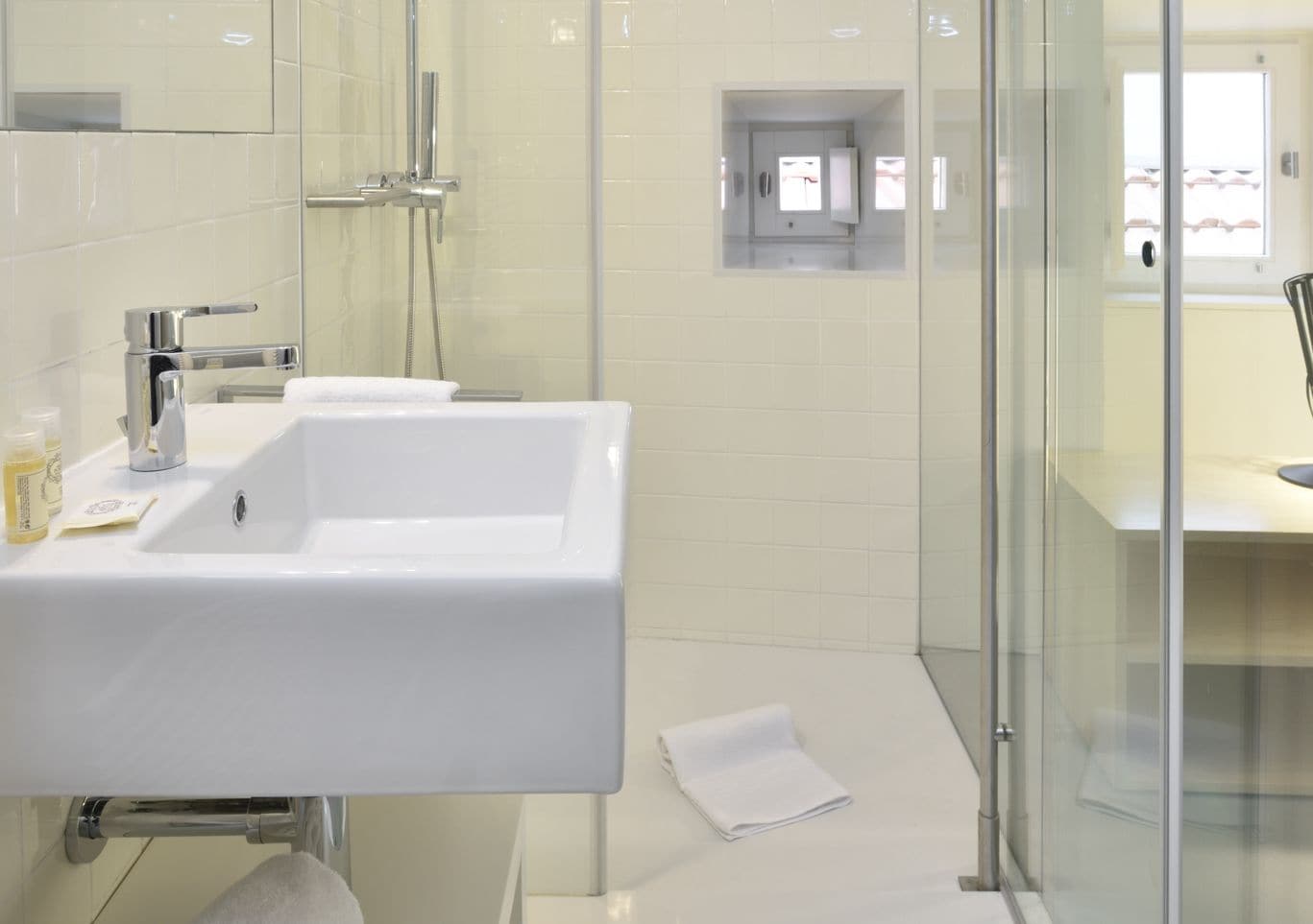 A modern bathroom with a white sink, a glass shower enclosure, and a small window.