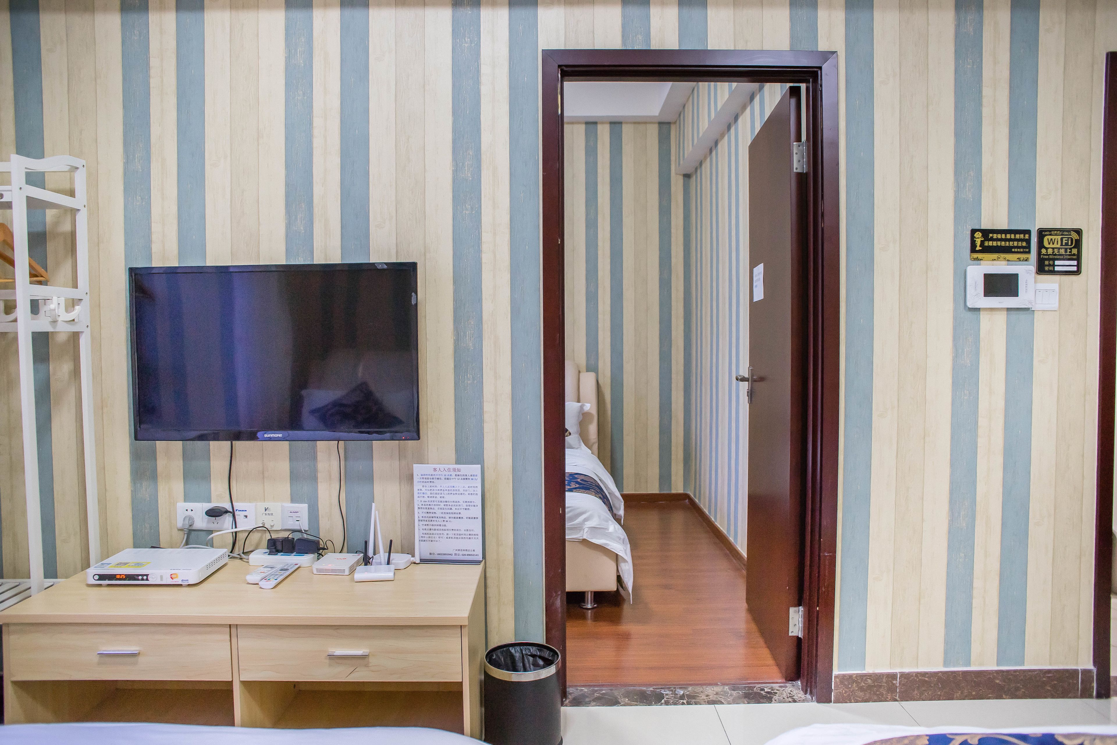 Ein Hotelzimmer mit Flachbildfernseher, Schreibtisch mit Computer, Mülleimer und Bett.