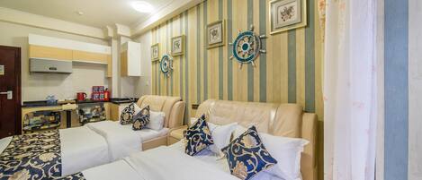 A hotel room with two beds, a sofa, a kitchenette, and nautical-themed wall decor.