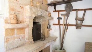 A stone fireplace with a shelf above it holding various kitchen utensils and a pot. - Masseria Nanni (Gallipoli)