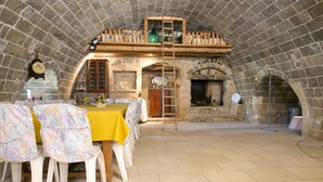 A dining area with a high stone ceiling, a wooden table with a yellow tablecloth, and floral chairs. - Masseria Nanni (Gallipoli)