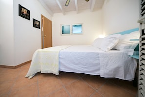 A bedroom with a bed, a door, a window, and a wall-mounted shelf. - Masseria Nanni (Gallipoli)