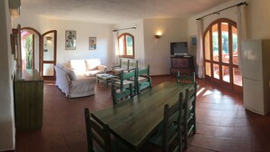 Un saló acollidor amb taula de dinar de fusta i cadires, un sofà, una televisió i un frigorífic.