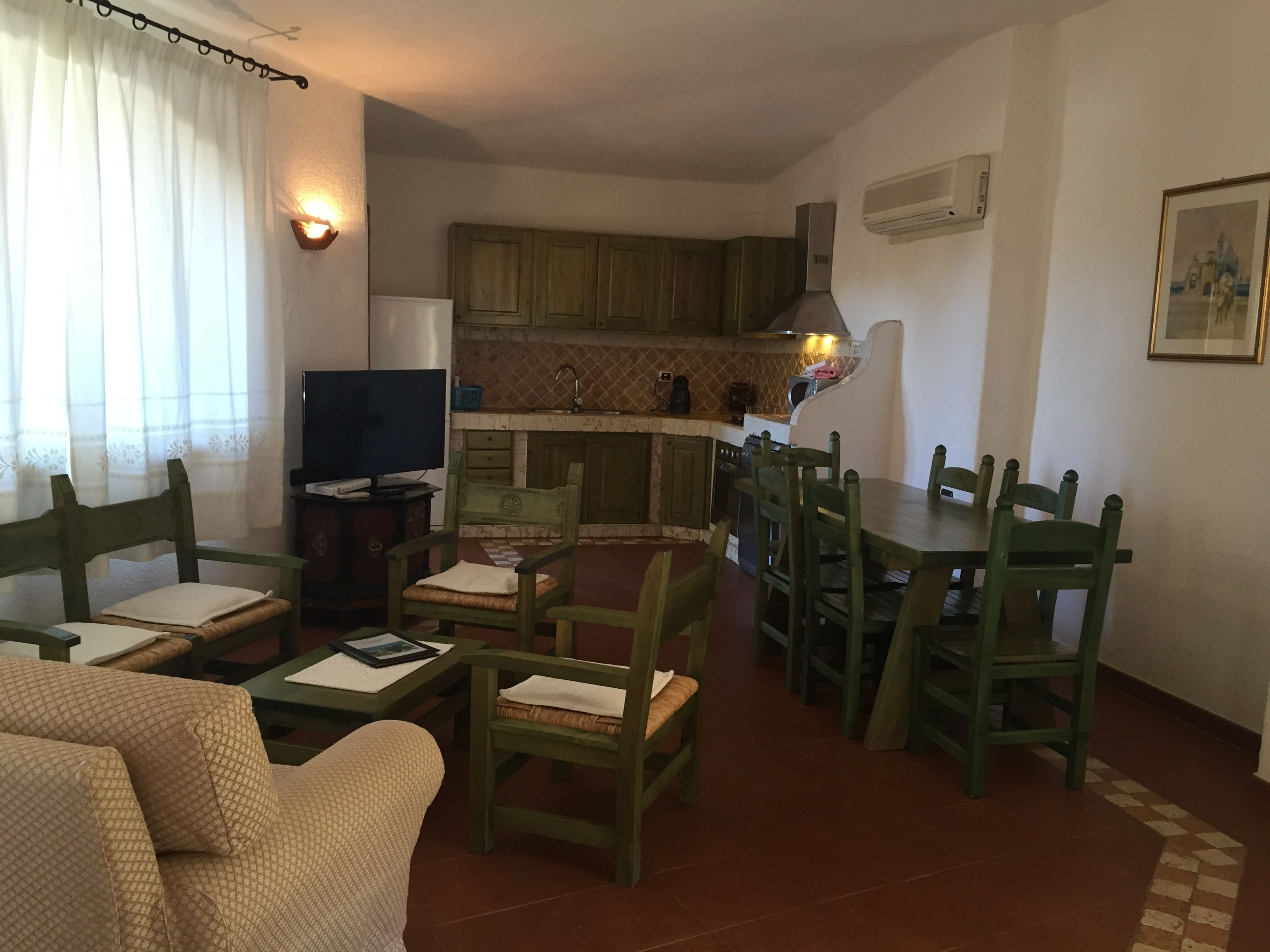 A cozy living room with a TV, a dining table with chairs, and a kitchen area with wooden cabinets and a stove.