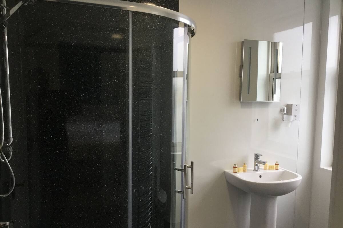 A modern bathroom with a glass-enclosed shower, a pedestal sink, and a mirror above the sink.