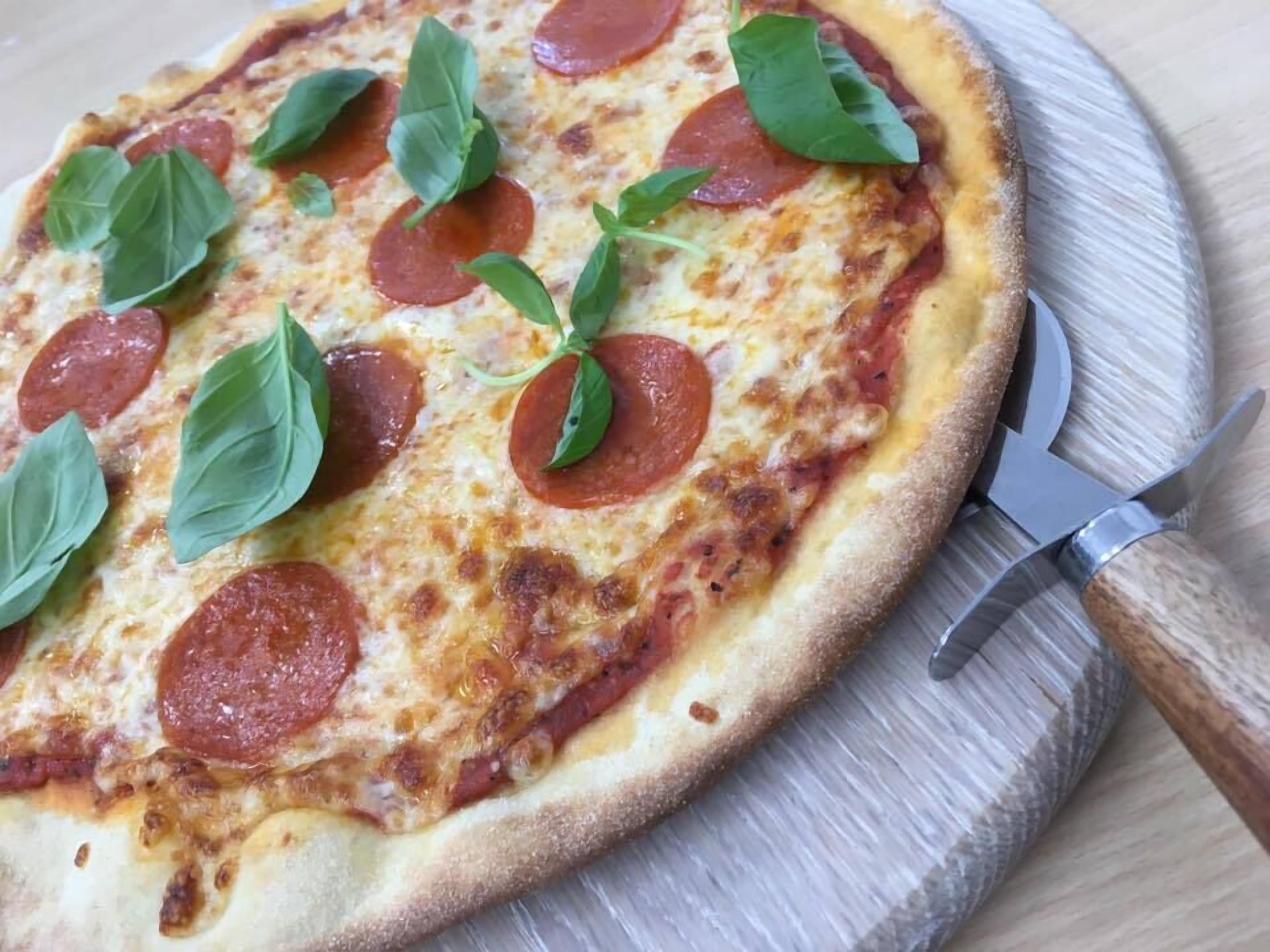 Una pizza con pepperoni y hojas de albahaca sobre una tabla de madera.