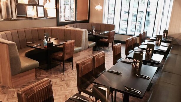 A restaurant with a modern interior, featuring a mix of seating options including booths and tables, and large windows providing natural light. - Oxgang Kitchen Bar & Rooms (Grangemouth)