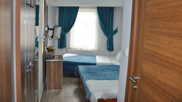 Quarto de hotel pequeno com duas camas, uma kitchenette e uma janela com cortinas.