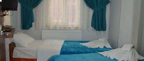 A room with two beds, a television on the wall, and a window with curtains.