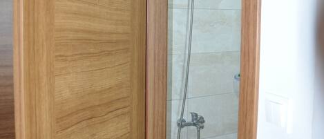 Puerta de madera que da a un área de ducha con puerta de cristal y suelo de baldosas.