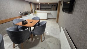 Uma cozinha compacta com eletrodomésticos modernos, uma área de refeições com cadeiras estofadas em cinza e uma TV de tela plana na parede.