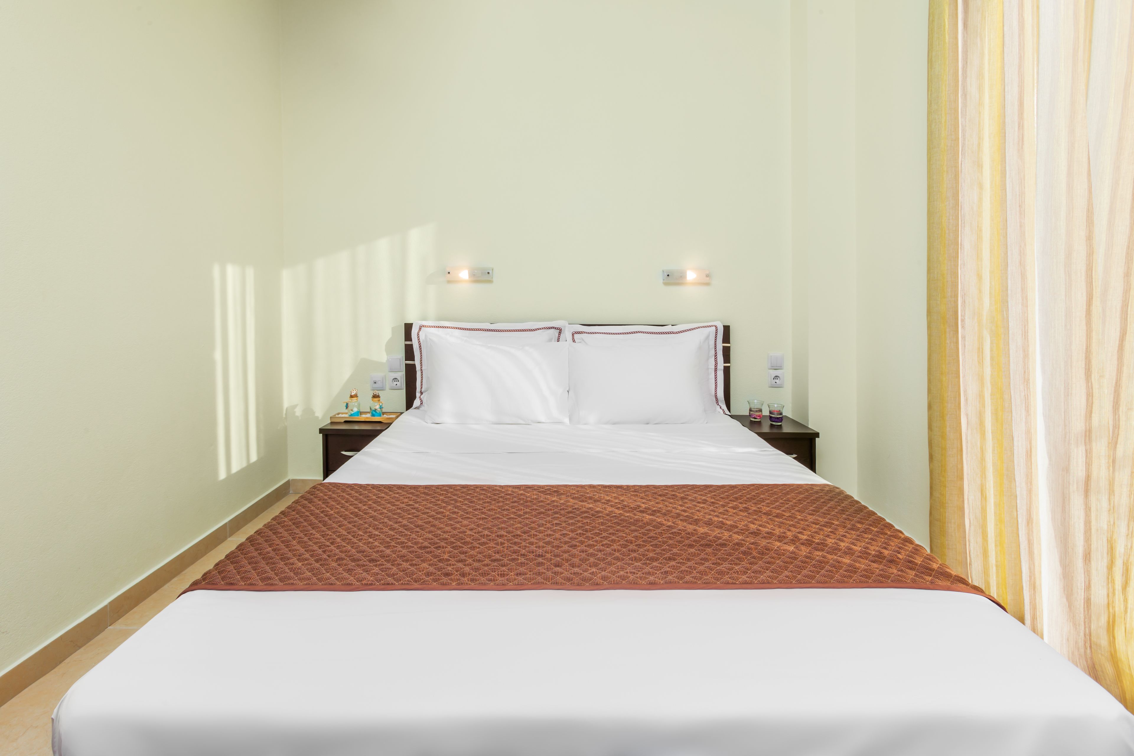 A hotel room with a bed, a nightstand, a lamp, and a wall-mounted light fixture.