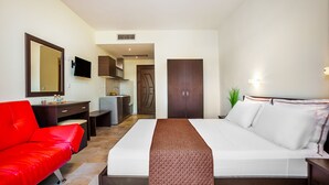 A hotel room with a bed, a red sofa, a desk, a TV, and a wardrobe. - Belohorizonte Fine Accommodation (Kassandra)