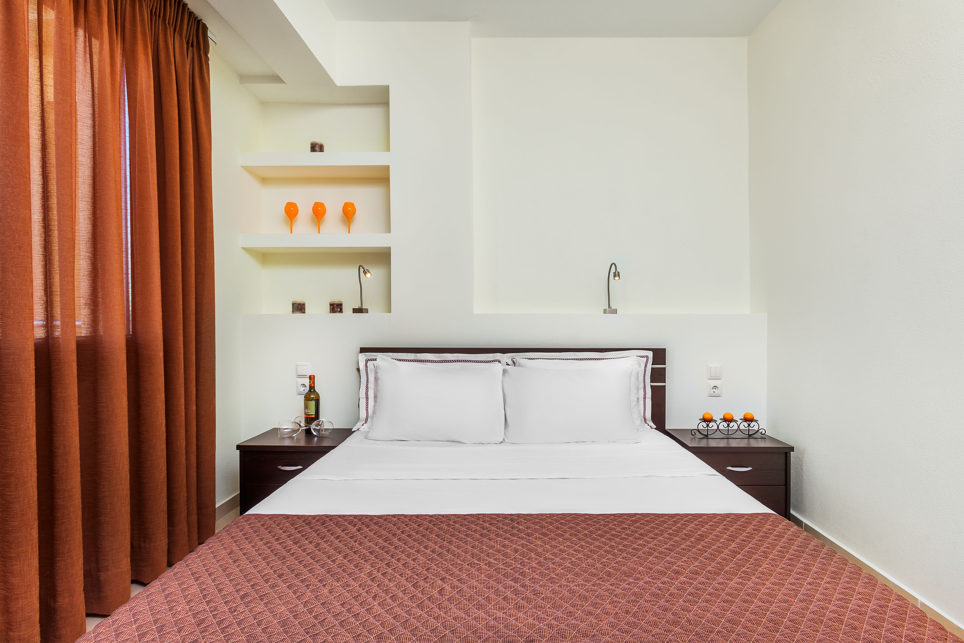 Een netjes ingerichte hotelkamer met een groot bed, een nachtkastje met een fles en een plank met decoratieve objecten.